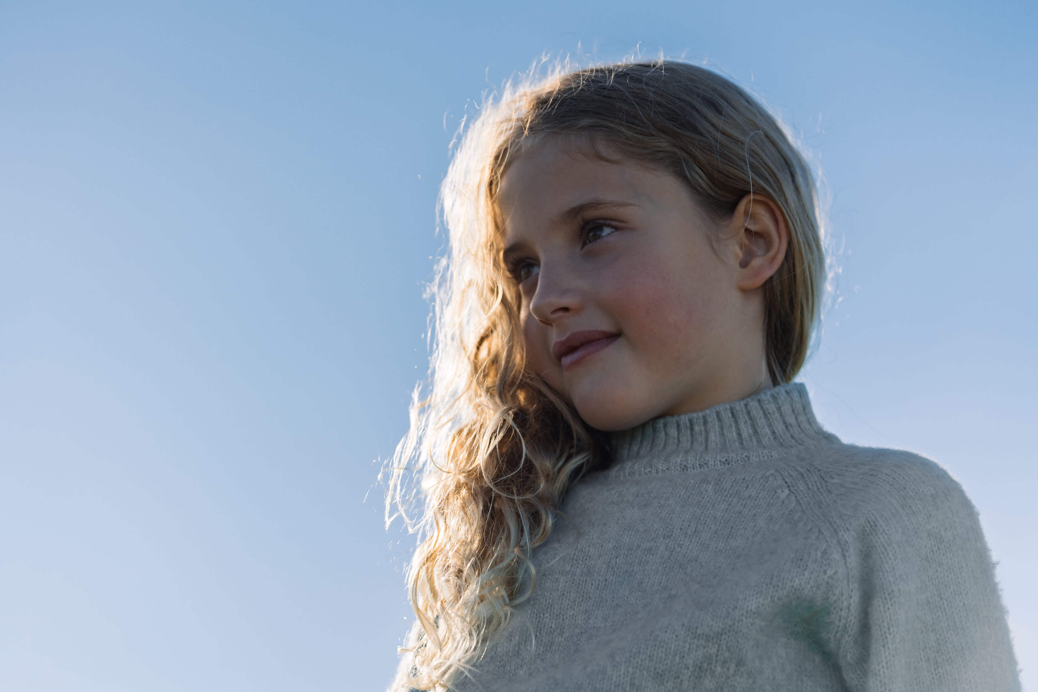 Petite fille blonde des cheveux bouclés qui regarde à gauche en souriant