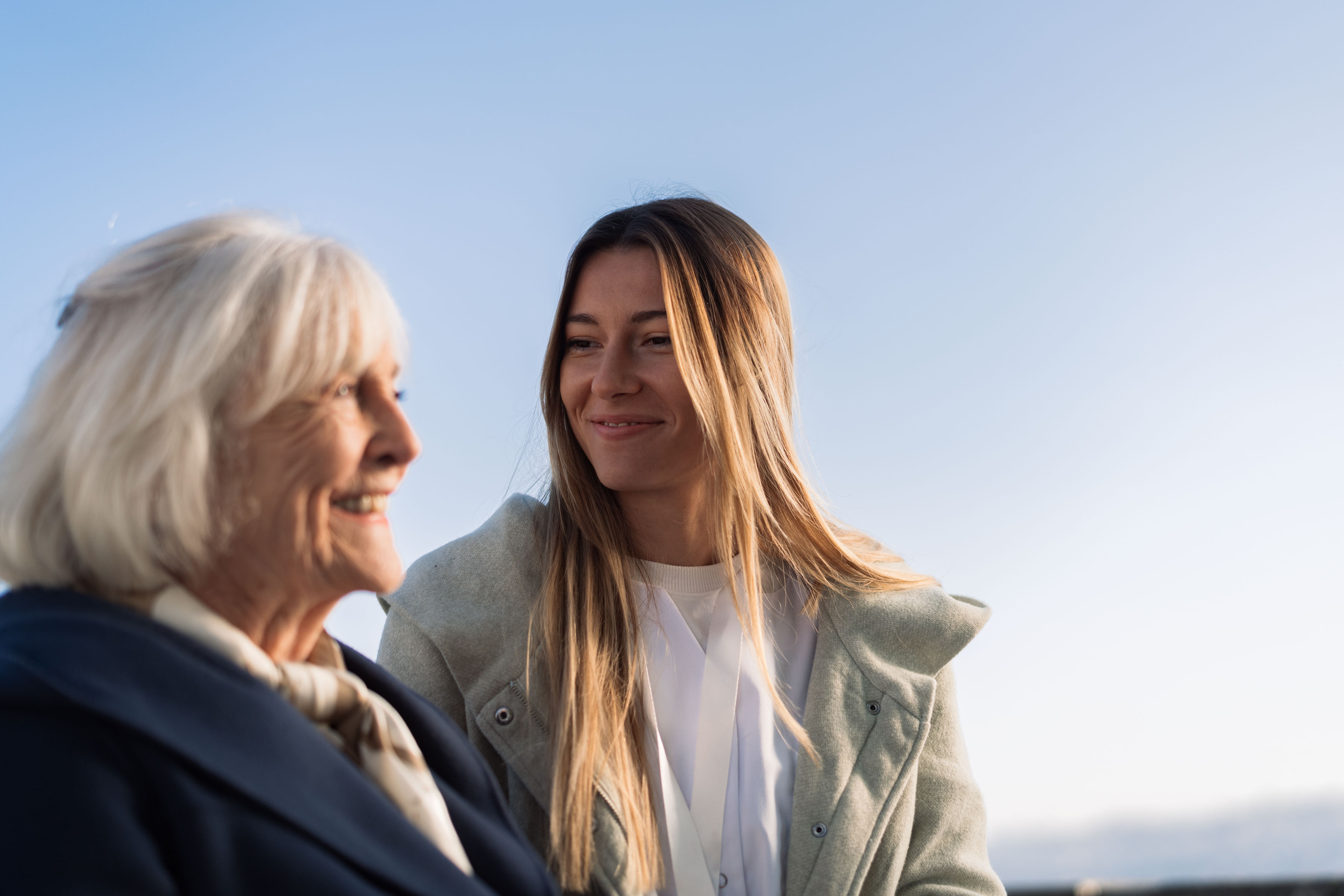 Jeune femme accompagnée d'une dame âgée, les deux en souriant et en regardant à droite